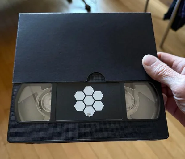 Тизерная VHS-кассета альбома «Inferno» с шестиугольным логотипом, в руке